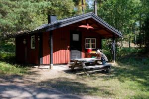 um homem sentado numa mesa de piquenique em frente a uma cabana em Grinda Stugby och Sea Lodge - Pensionat med kost & logi em Grinda