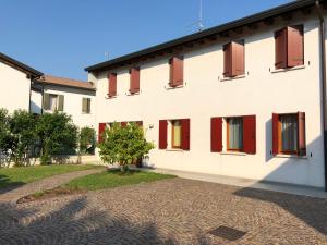 un bâtiment blanc avec des fenêtres rouges et un arbre dans l'établissement Cà Maria - Appartamento con Giardino, à San Polo di Piave