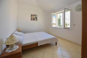 a white bedroom with a bed and a window at Apartments Luaniva 50m from the see in Novalja