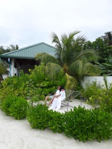Un uomo seduto su una panchina vicino a una palma di Sunrise Inn a Thoddoo