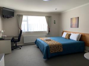 a bedroom with a bed and a desk and a window at High Peaks Hotel in Fox Glacier