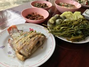 a table with a plate of fish and a plate of vegetables at Grandma's House in Nakhon Nayok