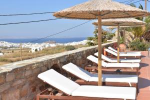 a row of lounge chairs with an umbrella and the ocean at Paradisia Villas in Naxos Chora