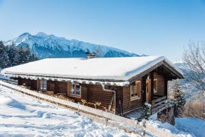 a wooden cabin covered in snow with mountains in the background at Ropferhof in Telfs-Buchen