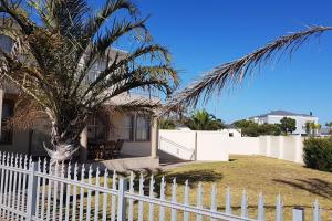 a white fence in front of a house with a palm tree at Fairway 2 Holiday Home in Langebaan