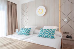 a bedroom with a white bed with two blue pillows at Grupotel Los Príncipes & Spa in Playa de Muro