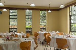 un comedor con mesas y sillas blancas y ventanas en LIA Hotel & Training Centre, en Nairobi