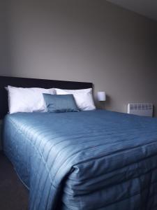 un grande letto con coperta blu e cuscini bianchi di Northpark Motel a Timaru