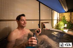 a man in a bath tub holding a cell phone at Konjaku-So Dotonbori Garden SPA Stay in Osaka