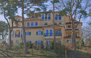 a large yellow building with blue windows and trees at Baabe Gruene Duene Fewo Mee_h_rbli in Baabe