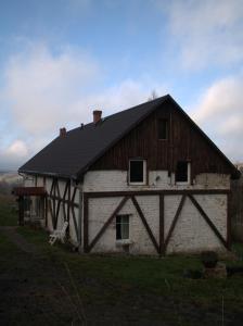an old barn with a black roof on a field at Dziki domek in Sierpnica