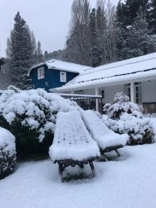 dos bancos cubiertos de nieve frente a una casa en Hostería La Casa de Eugenia en San Martín de los Andes