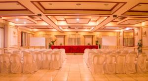 um salão de banquetes com cadeiras brancas e uma mesa vermelha em Benguet Prime Hotel em Baguio