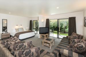 Kauri Park Motel في كيريكيري: غرفة نوم بسرير واريكة وتلفزيون