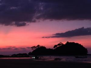 a sunset on the beach with a island in the water at Sea Rounding in Ko Phra Thong
