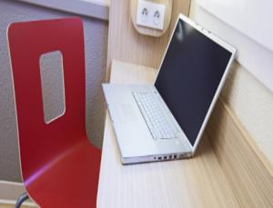 un ordinateur portable assis sur un bureau à côté d'une chaise rouge dans l'établissement Premiere Classe Saint Etienne - Aéroport Bouthéon, à Andrézieux-Bouthéon