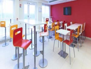 Cette chambre est dotée de tables, de chaises et d'un mur rouge. dans l'établissement Premiere Classe Saint Etienne - Aéroport Bouthéon, à Andrézieux-Bouthéon
