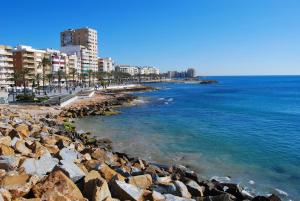einen Strand mit Felsen und Gebäuden und dem Meer in der Unterkunft RUMOHOLIDAYS Spacious 3 bedrooms apartment Playa del Cura in Torrevieja
