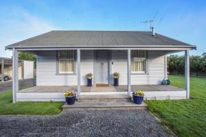 une petite maison blanche dotée d'une terrasse couverte avec deux plantes en pot dans l'établissement The Vicarage Martinborough, à Martinborough