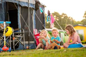 
three children sitting on the grass next to a tent at BIG4 Traralgon Park Lane Holiday Park in Traralgon
