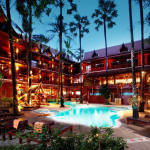 un hotel con piscina y palmeras por la noche en Royal Phawadee Village Patong - SHA Plus, en Patong Beach