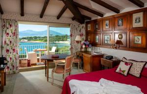 a bedroom with a bed and a desk and a balcony at Hotel Le Maquis in Porticcio