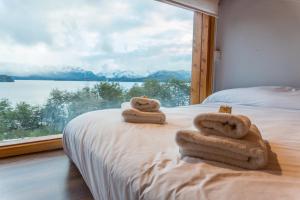 1 cama con toallas y ventana grande en BOG Atardeceres del lago - piscina climatizada y vistas al lago en Villa La Angostura