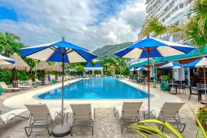 a swimming pool with chairs and blue umbrellas at Andaman Sea View Apartment - Patong Beach in Patong Beach