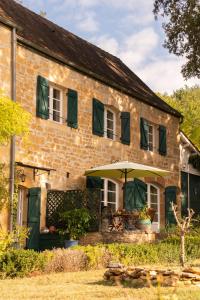 an old brick house with a table and an umbrella at Maison de charme à 5 km de Sarlat avec piscine in Carsac-Aillac