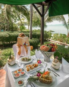 a woman reading a book while sitting at a table with food at Bo Phut Resort and Spa - SHA Plus in Bophut