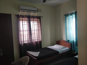a small bedroom with a bed and two windows at Tulip Suites in Coimbatore