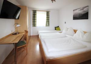 a room with two beds and a desk and a television at Landhaus Lindorfer in Grossarl