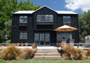 a black house with a table and an umbrella at Black Walnut Cottage in Havelock North