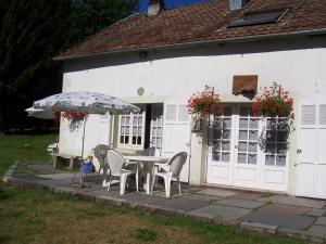 a white house with a table and chairs and an umbrella at Gîtes La Coquille in Ternuay-Melay-et-Saint-Hilaire