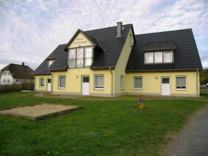 une maison jaune avec un toit noir sur une cour dans l'établissement Mobilcamp Heringsdorf _Haus Trifte, à Heringsdorf