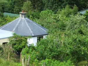 a white house with a black roof with trees at Drombrow Cottage in Bantry