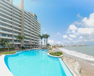 a swimming pool next to a beach with a large building at Lindo Departamento al pie de playa Edificio TORRE OCEÁNICA in Salinas