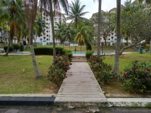 a wooden path in a park with palm trees and flowers at Haji Din Cocobay Condo in Port Dickson