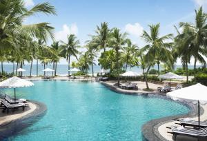 a pool with palm trees and chairs and umbrellas at Taj Bentota Resort & Spa in Bentota