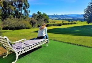 a woman sitting on a bench in a field at Pear Tree Cottage-Underberg in Underberg
