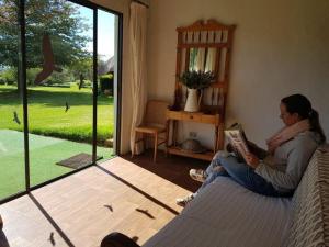 une femme assise sur un lit en train de lire un livre dans l'établissement Pear Tree Cottage-Underberg, à Underberg