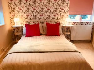 a bedroom with a large bed with two red pillows at Wisteria Cottage in Gravesend