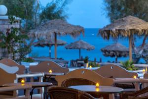 a restaurant with tables and straw umbrellas and the ocean at Veggera Beach Hotel in Perissa