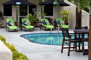 einen Pool mit Stühlen, Tischen und einem Sonnenschirm in der Unterkunft Coral Sands Apartments in Rarotonga