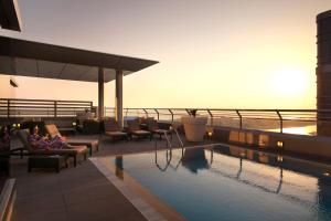 uma piscina no telhado de um hotel com pessoas sentadas em cadeiras em Centro Capital Centre By Rotana em Abu Dhabi