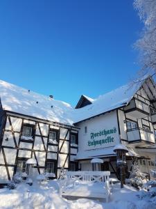 un edificio cubierto de nieve con mesas y bancos en Hotel - Restaurant - Café Forsthaus Lahnquelle en Netphen