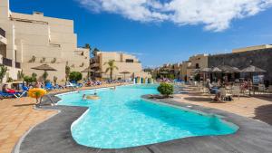uma piscina num resort com pessoas sentadas em cadeiras em Blue Sea Apartamentos Costa Teguise Gardens em Costa Teguise