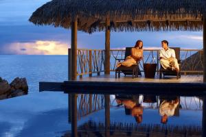two people sitting in chairs on a porch overlooking the ocean at Tadrai Island Resort in Mana Island