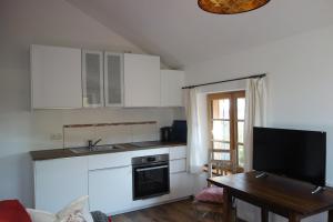 cocina con armarios blancos, mesa y TV en Appartement - Ferienwohnung - FeWo Heuboden en Emmering