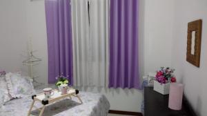 a bedroom with purple and white curtains and a table at Stúdio Petrópolis, Alameda das Pedras in Petrópolis